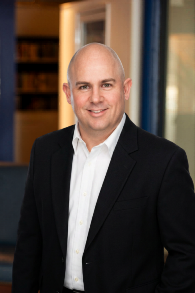 Professional headshot of a Two Capitols Consulting team member Dave in a black suit, indoor setting